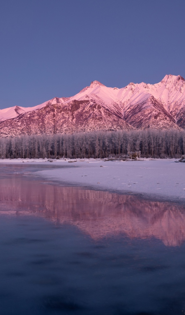 The moon over the snow-capped mountains is reflected in the icy lake