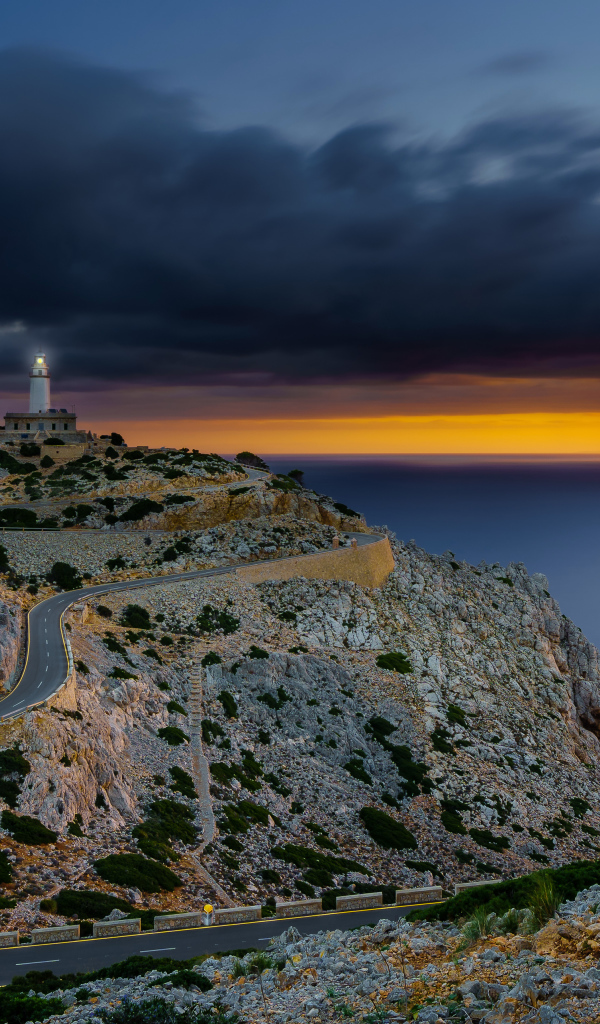 Извилистая дорога ведет к маяку на краю скалы под пасмурным небом