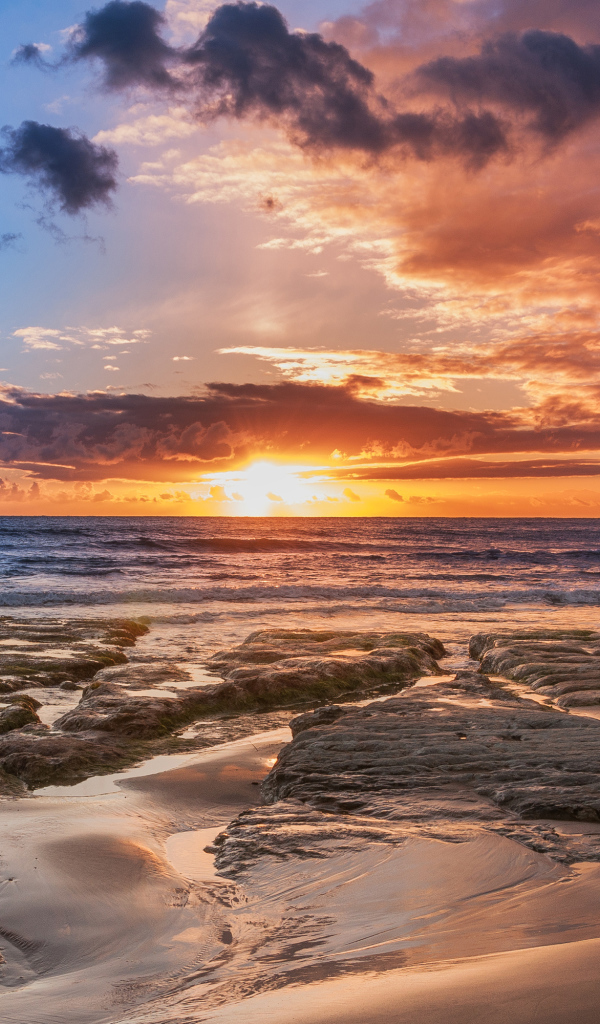 Мокрый песок и камни на берегу океана на закате солнца
