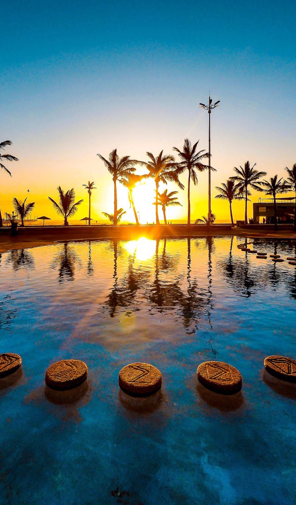 Закат солнца на тропическом пляже на фоне бассейна