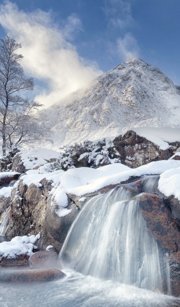 Водопад стекает с камней на фоне заснеженной горы