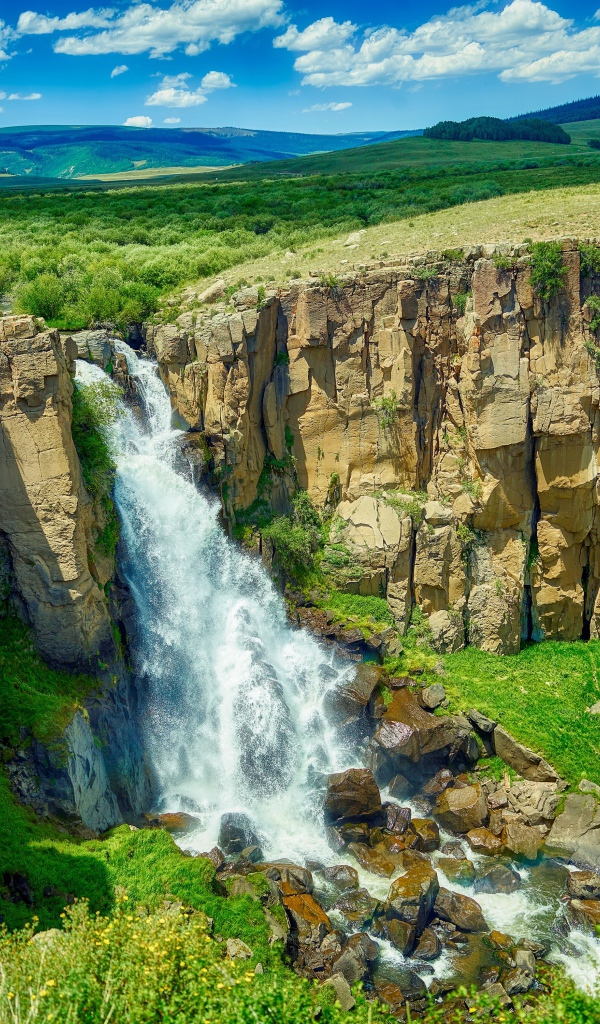 Быстрая вода водопада стекает по утесу на фоне голубого неба