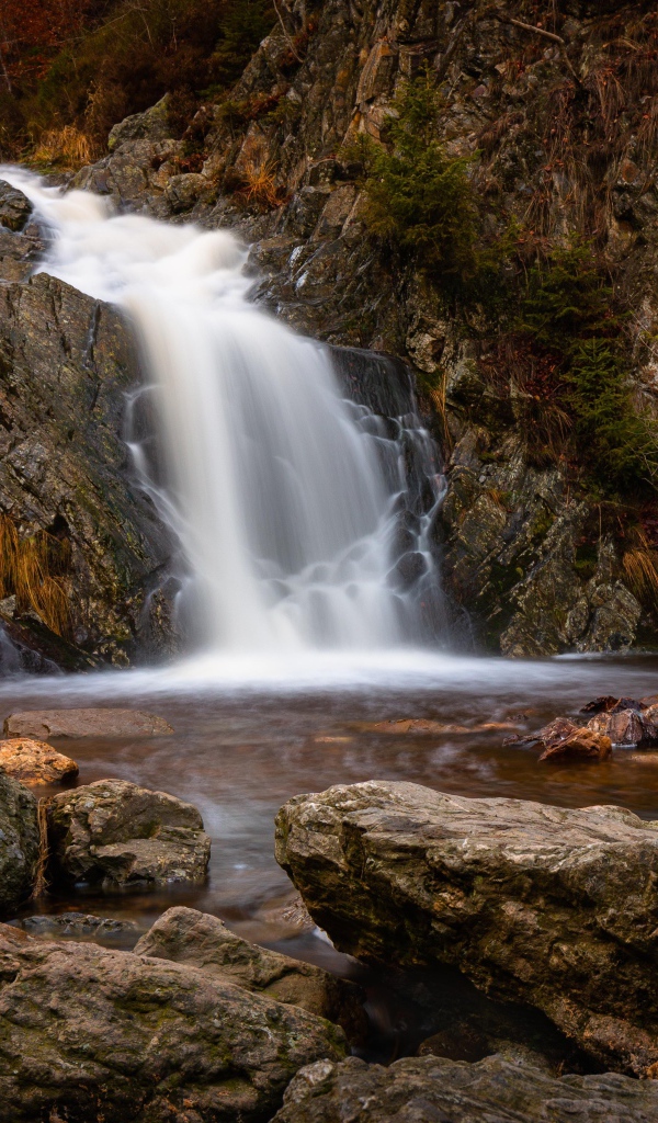 Быстрая вода водопада стекает по камням в горную реку