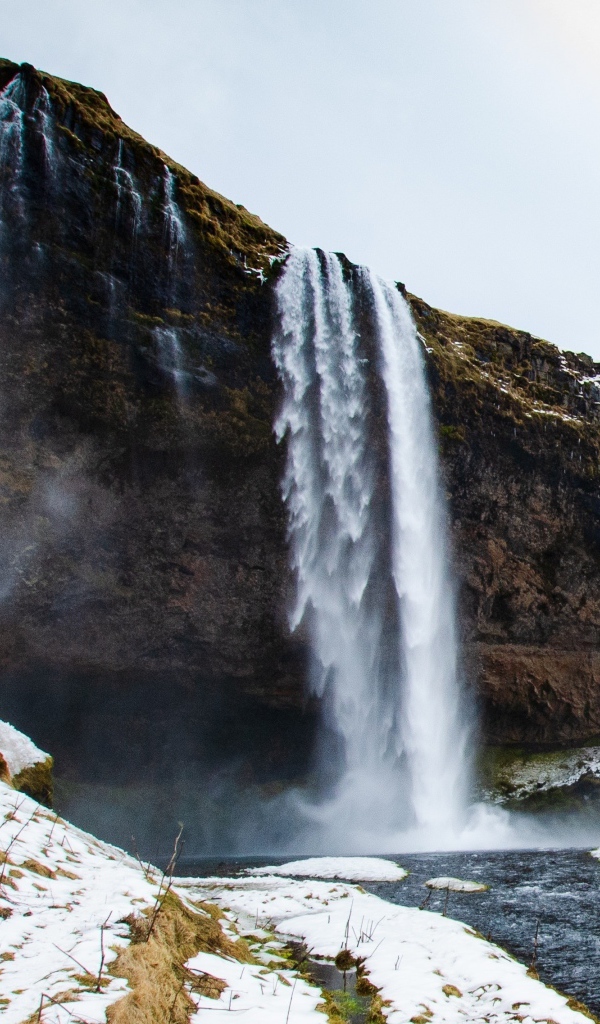 Водопад стекает со скалы в реку с покрытыми снегом берегами