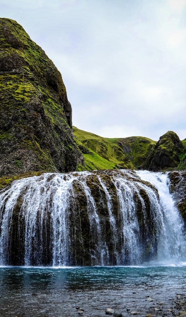 Белая вода водопада стекает по покрытым мхом скалам