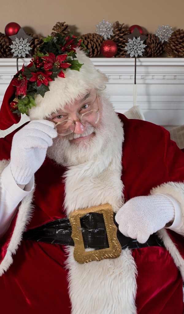 Санта Клаус в очках сидит у камина у новогодней елки