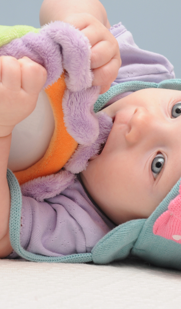 Младенец в шапке грызет мягкую игрушку