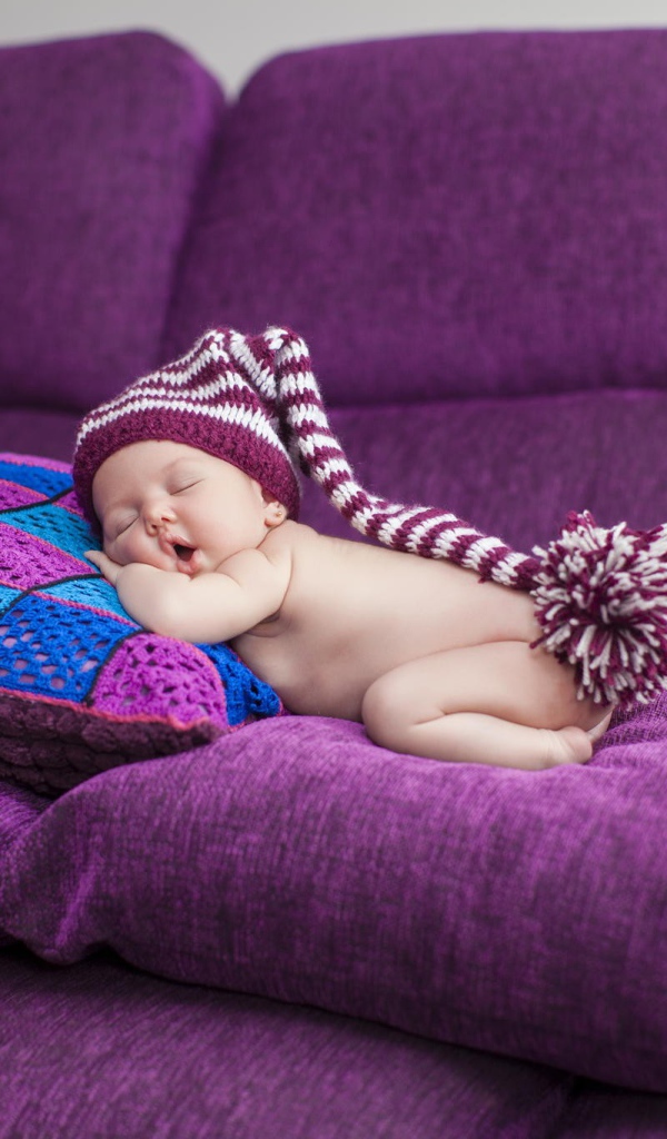 Маленький ребенок в большой шапке спит на фиолетовых подушках