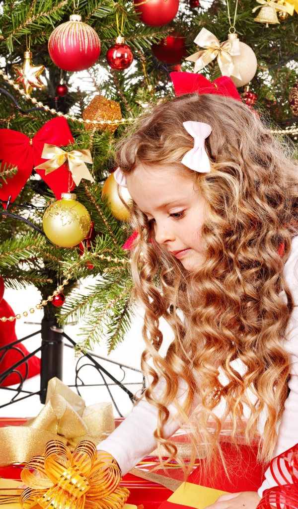 Красивая маленькая девочка смотрит подарки под елкой на новый год 