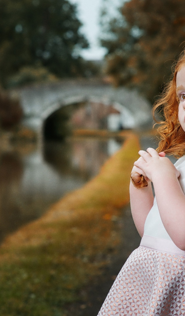 Красивая рыжеволосая девочка у реки в парке 