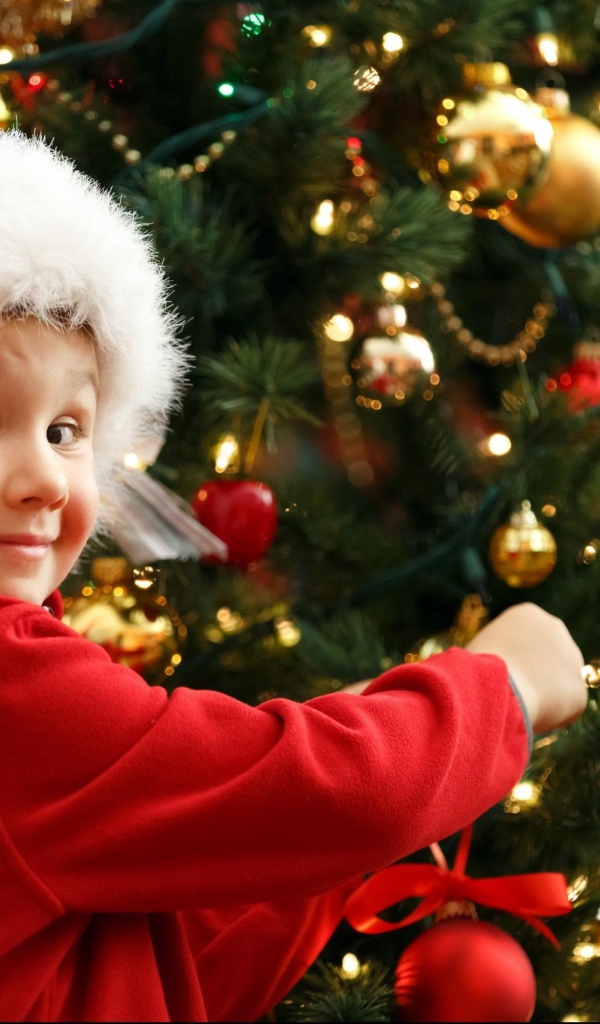 Мальчик в шапке Санта Клауса наряжает елку