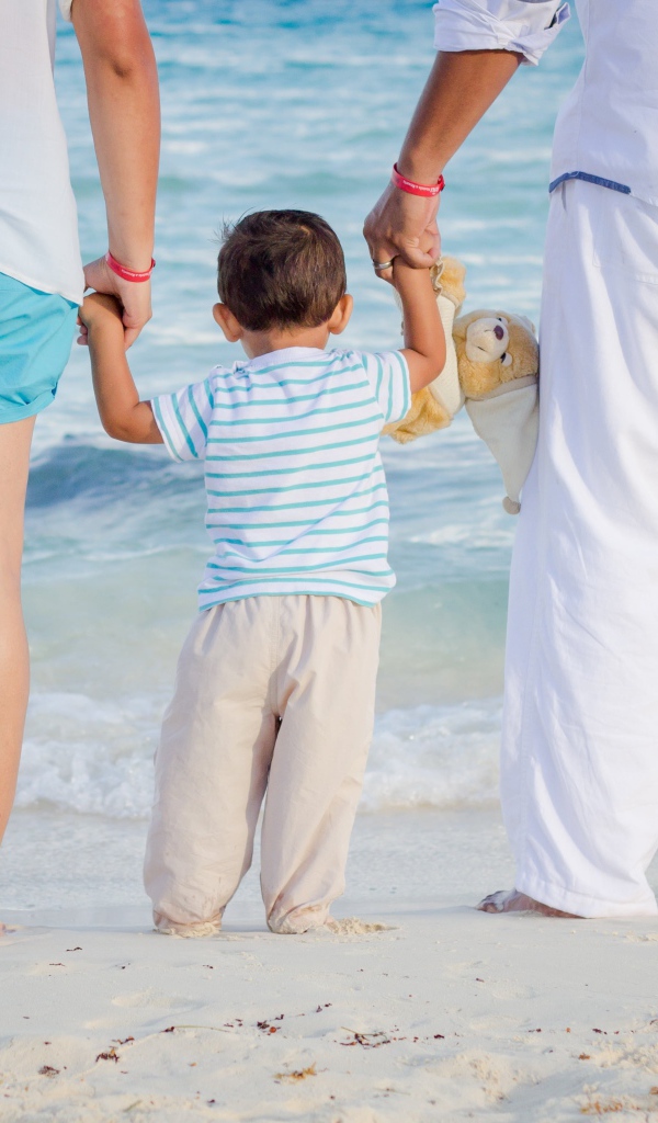 Семья с маленьким ребенком идет по пляжу