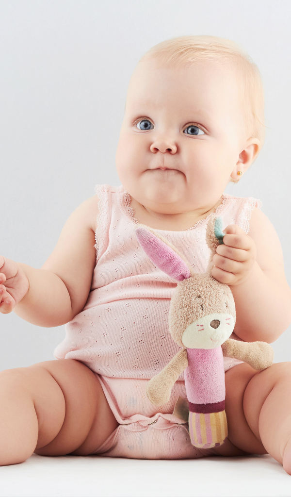 Смешной малыш с игрушкой сидит на сером фоне