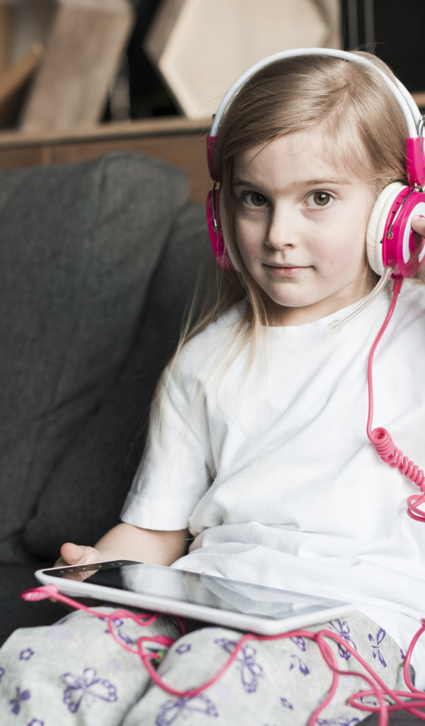 Девочка сидит на диване в наушниках  и с планшетом