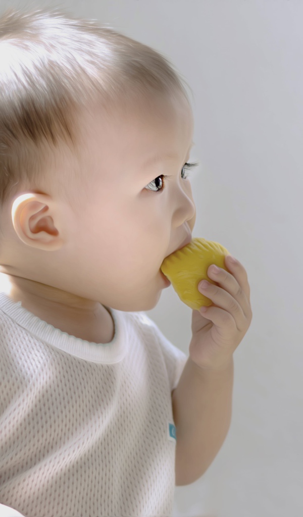 Маленький ребенок грызет игрушку на сером фоне
