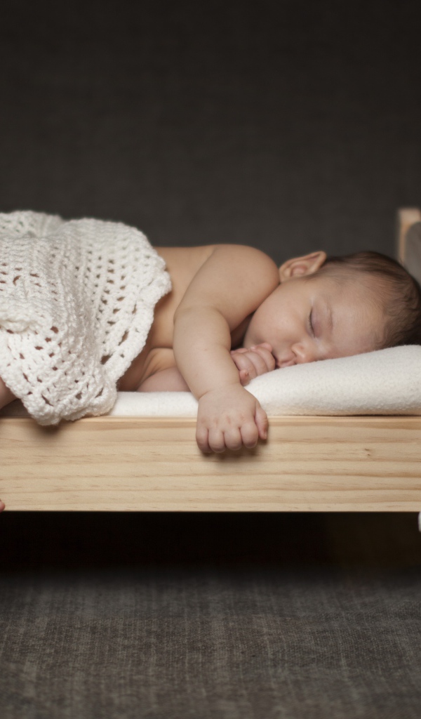 Маленький ребенок спит на деревянной кроватке с игрушкой