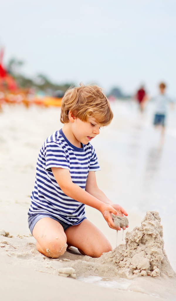 Маленький мальчик строит замок из песка на пляже