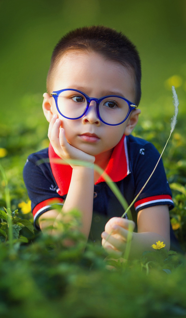 Маленький мальчик в очках лежит на зеленой траве