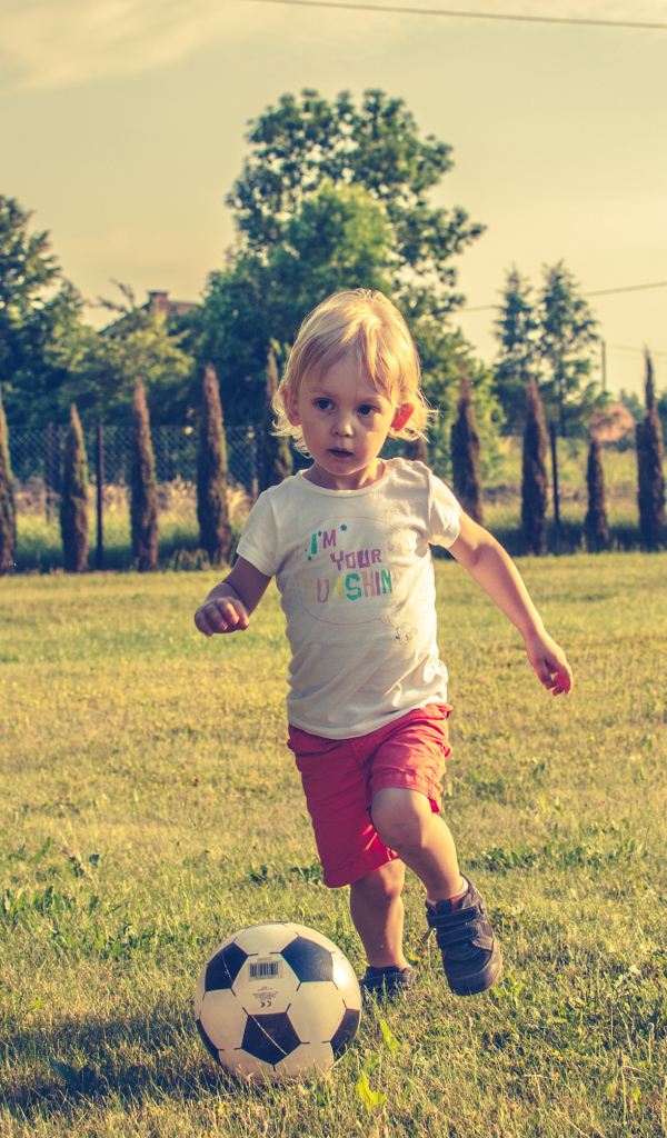 Маленький мальчик играет в футбол на зеленой траве