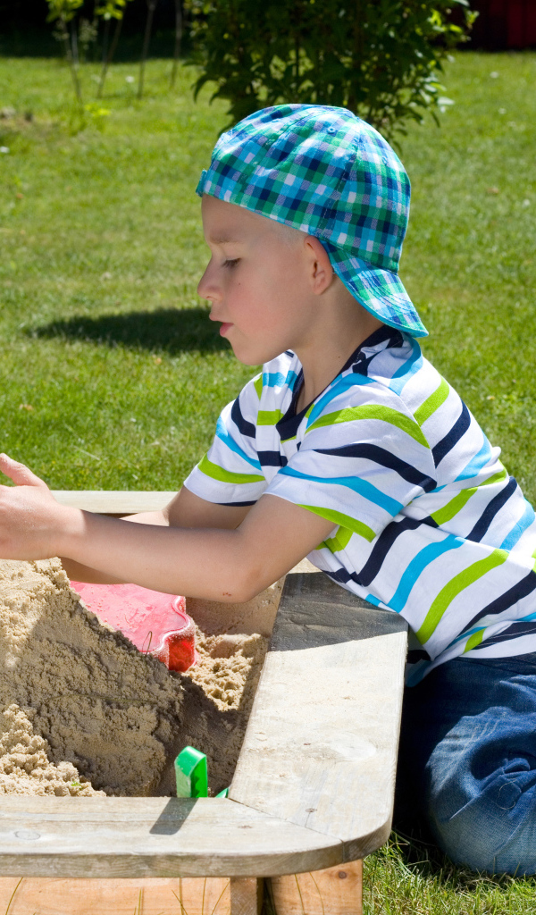 Маленький мальчик играет в песке на зеленой траве
