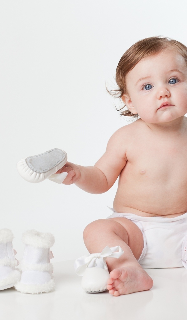 Маленький забавный голубоглазый малыш с обувью на белом фоне