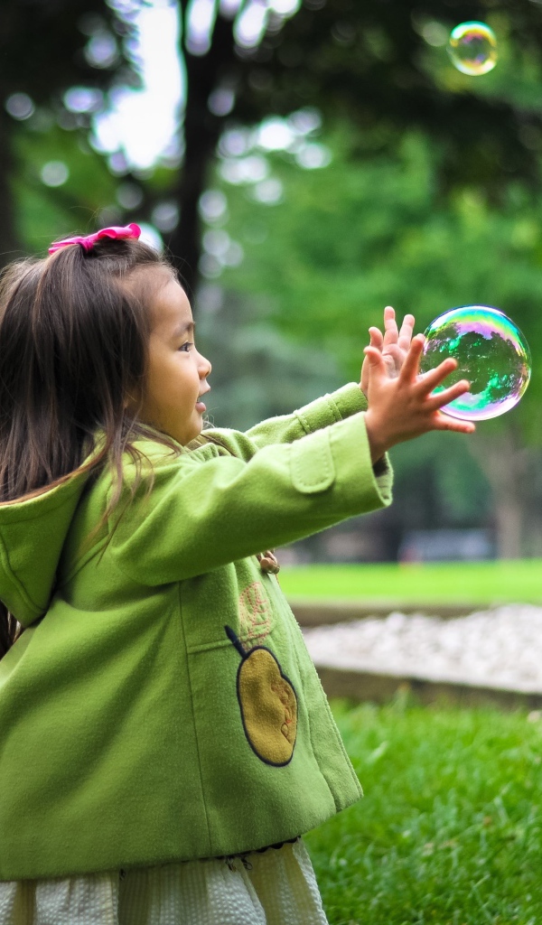 Маленькая девочка ловит мыльные пузыри на зеленой траве