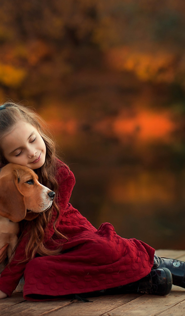 Маленькая девочка обнимает собаку породы бигль на мосту