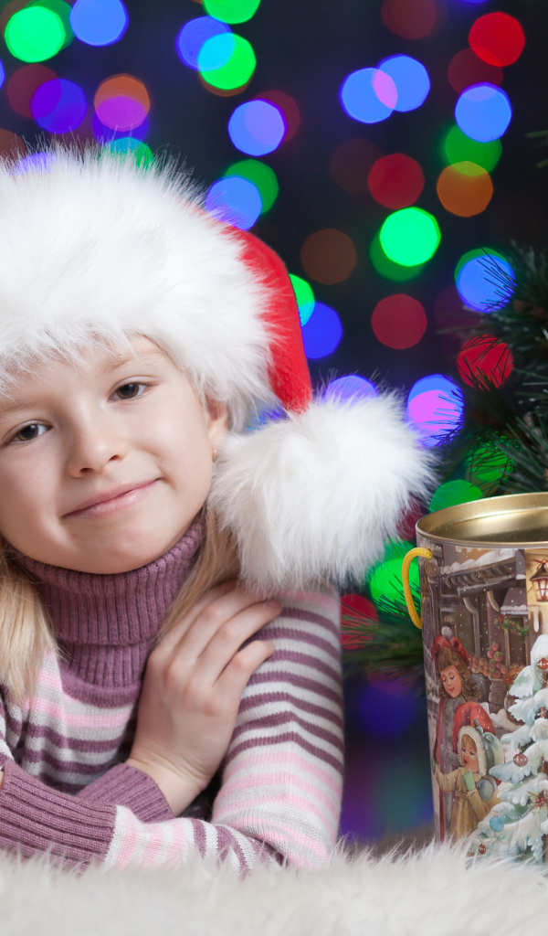 Маленькая девочка в новогодней шапке у елки