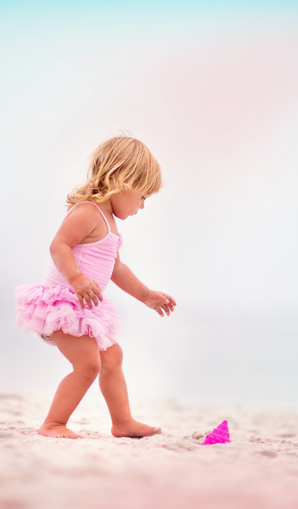 Маленькая девочка в розовом купальнике на песке