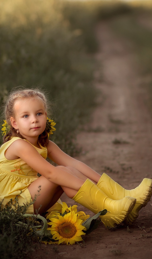 Маленькая девочка в желтом платье сидит на земле с подсолнухами