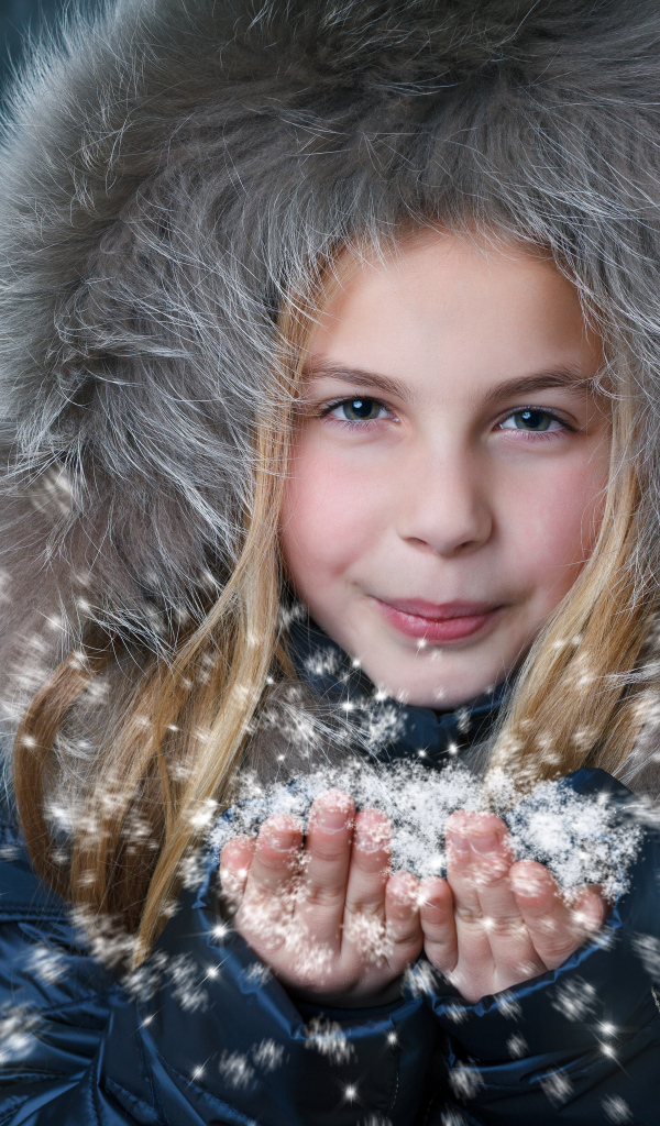 Маленькая девочка в капюшоне сдувает снежинки с ладоней