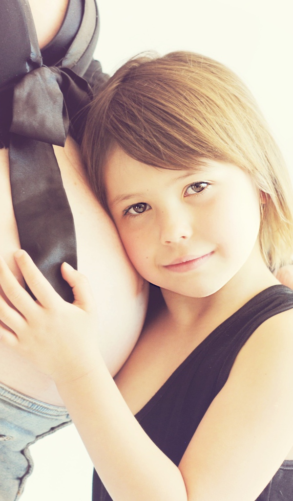 Маленькая девочка прислоняется к животу беременной женщины