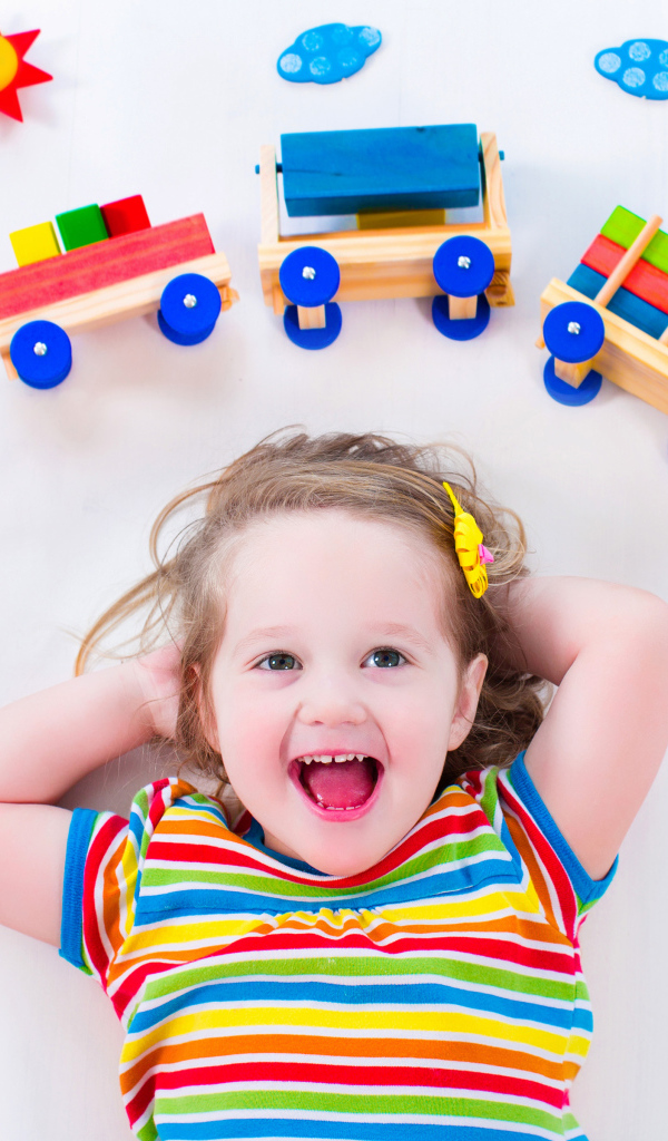 Маленькая девочка на сером фоне с игрушечным паровозом 