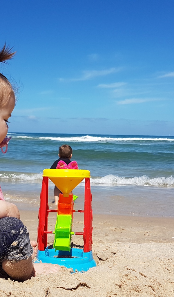 Маленькая девочка играет на песке у моря