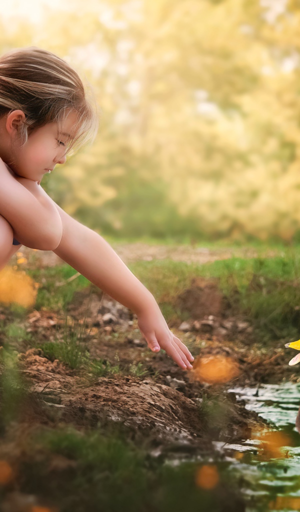 Маленькая девочка играет с уточкой в воде