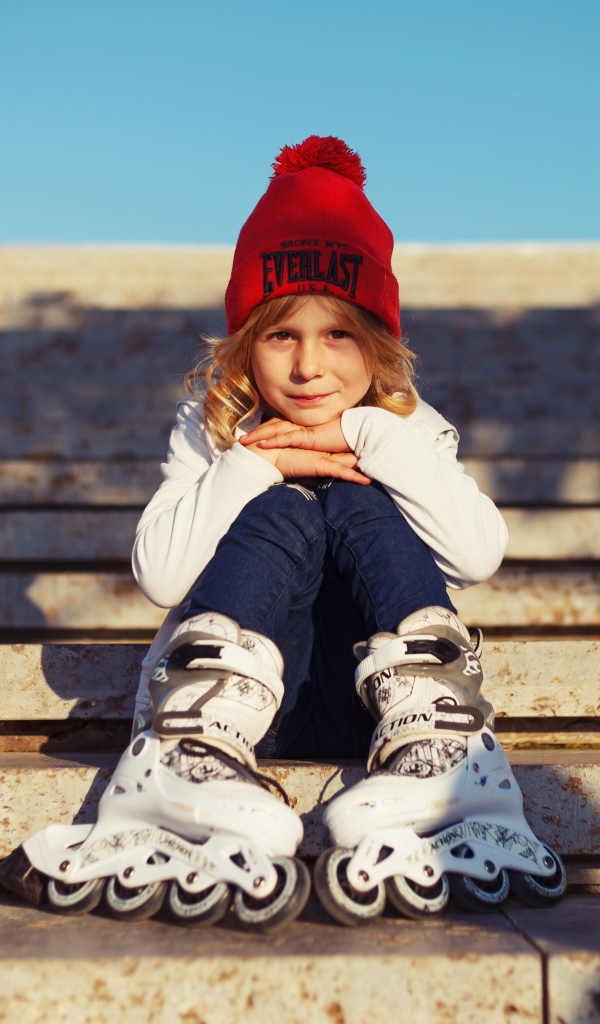 Маленькая девочка в роликах сидит на ступеньках 