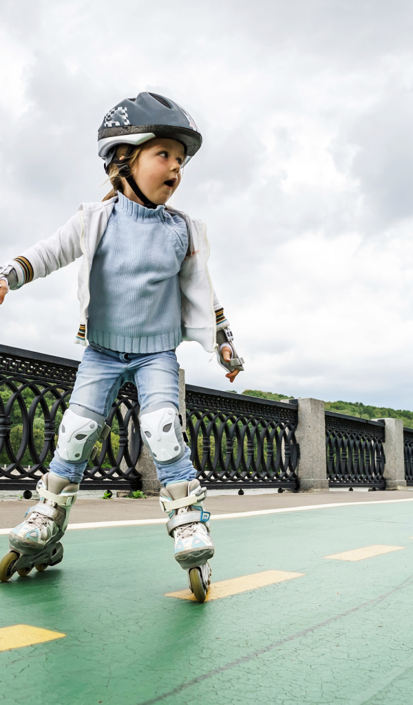 Маленькая девочка катается по мосту на роликах