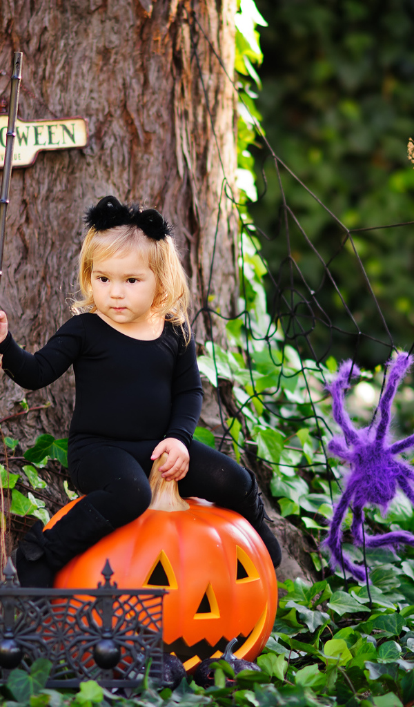 Маленькая девочка сидит на тыкве в лесу в костюме на Хэллоуин 