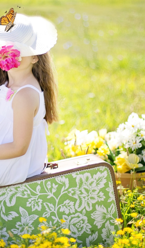 Маленькая девочка сидит на чемодане на поле с цветами