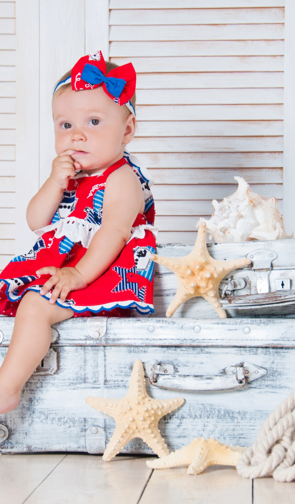 Маленькая девочка сидит на чемодане с морскими звездами