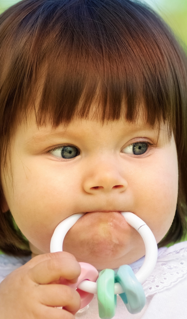 Маленькая девочка с погремушкой во рту