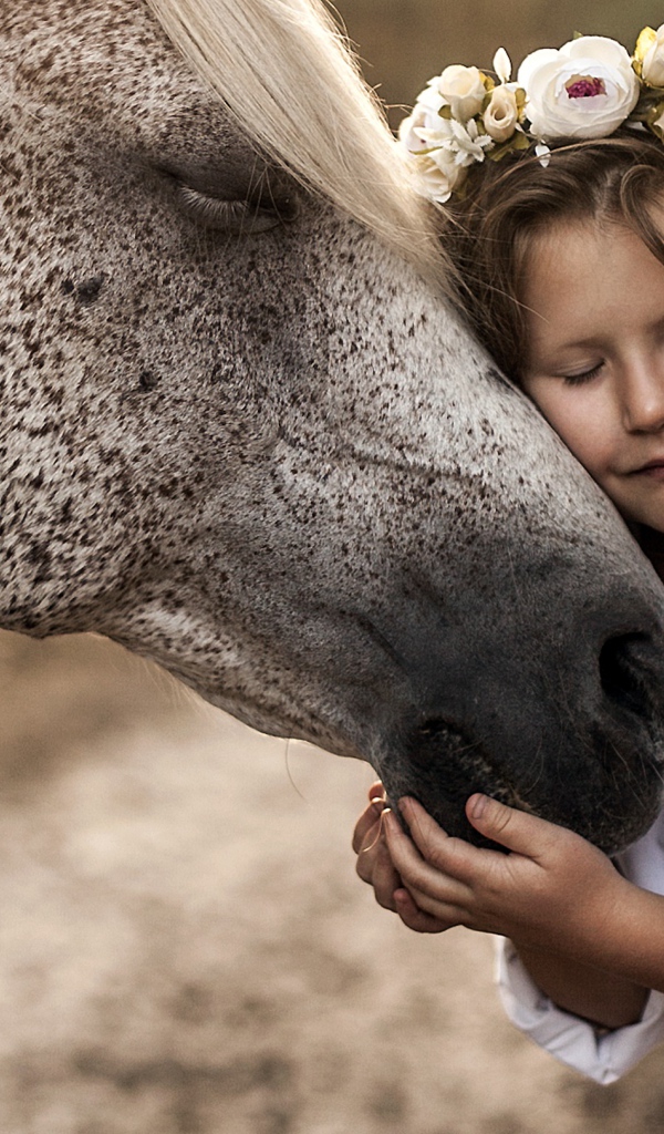 Маленькая девочка с венком на голове обнимает лошадь