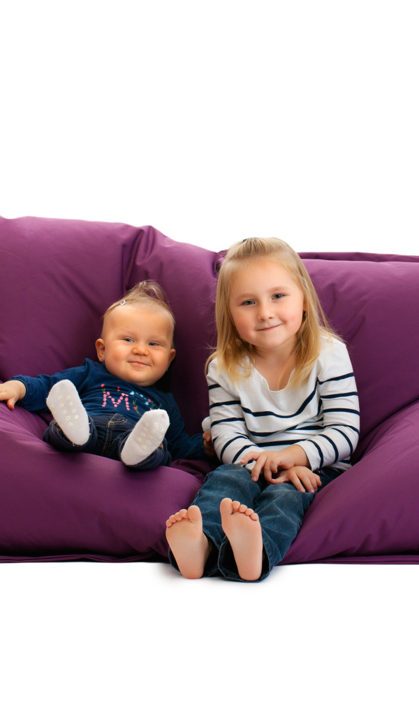 Маленькие девочки сидят на мягкой подушке на белом фоне