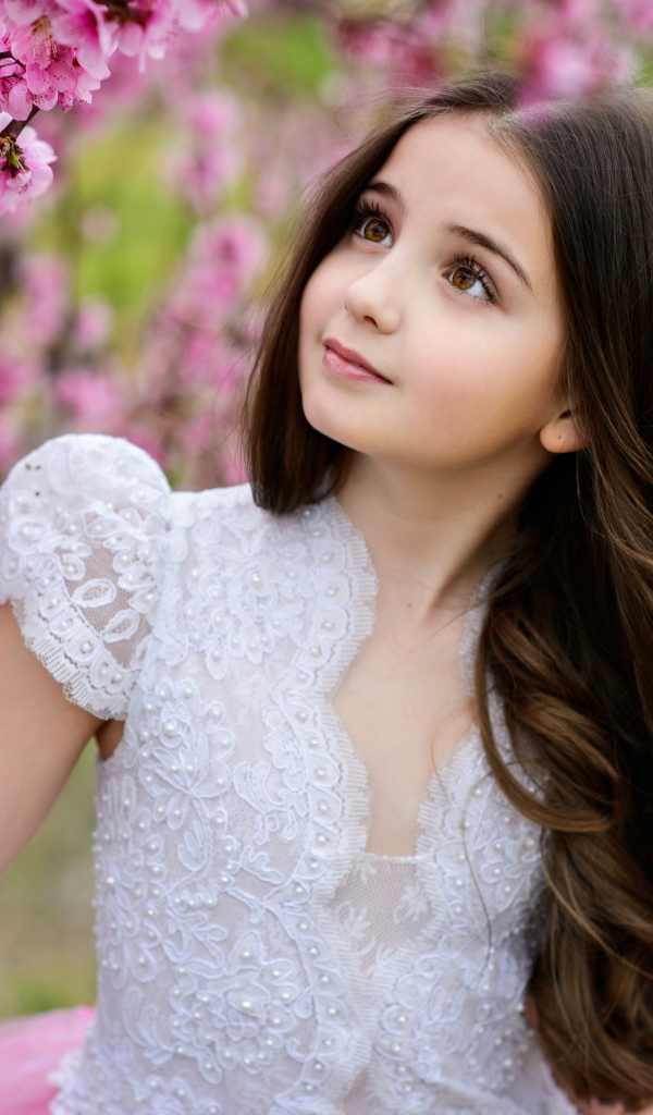 Маленькая длинноволосая девочка у дерева с розовыми цветами