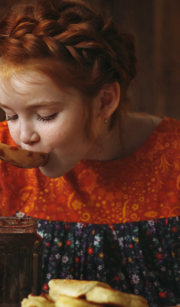 Маленькая рыжеволосая девочка пробует варенье