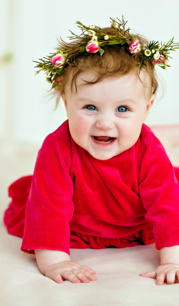 Маленькая улыбающаяся девочка в красном платье с венком на голове