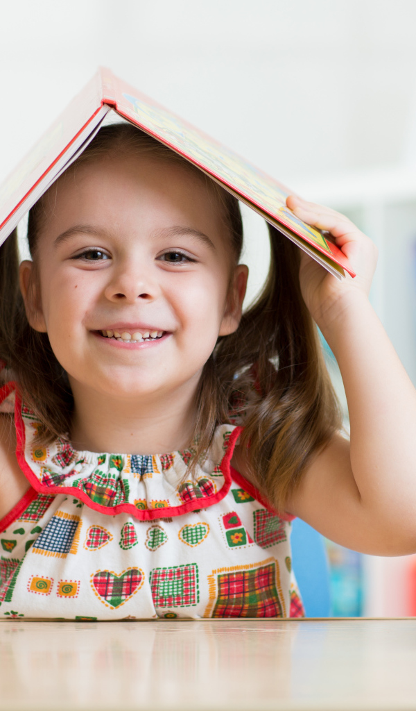 Маленькая улыбающаяся девочка с книгой на голове