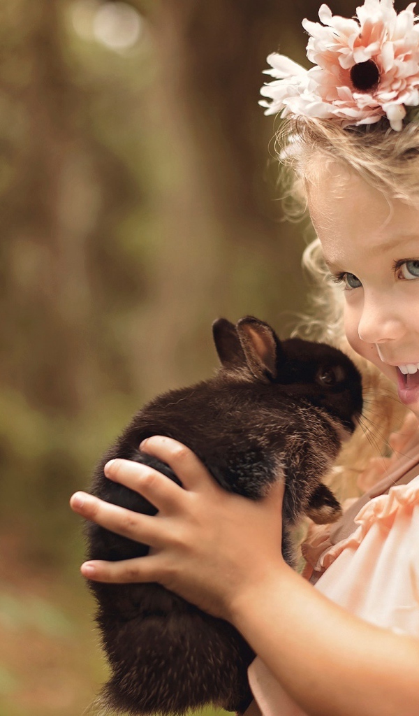 Маленькая улыбающаяся девочка с венком на голове держит кролика