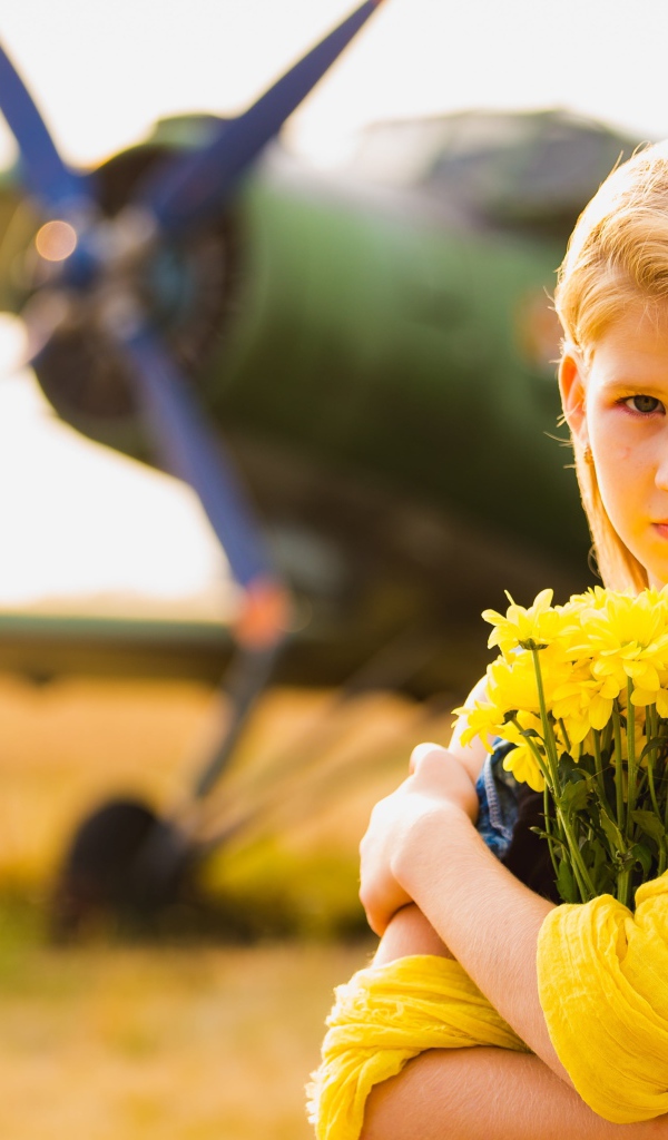 Длинноволосая девочка с букетом желтых хризантем на фоне самолета 