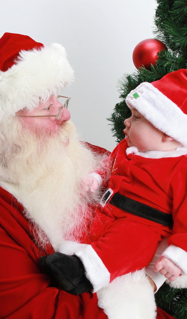 Дед Мороз держит на руках маленького ребенка у елки